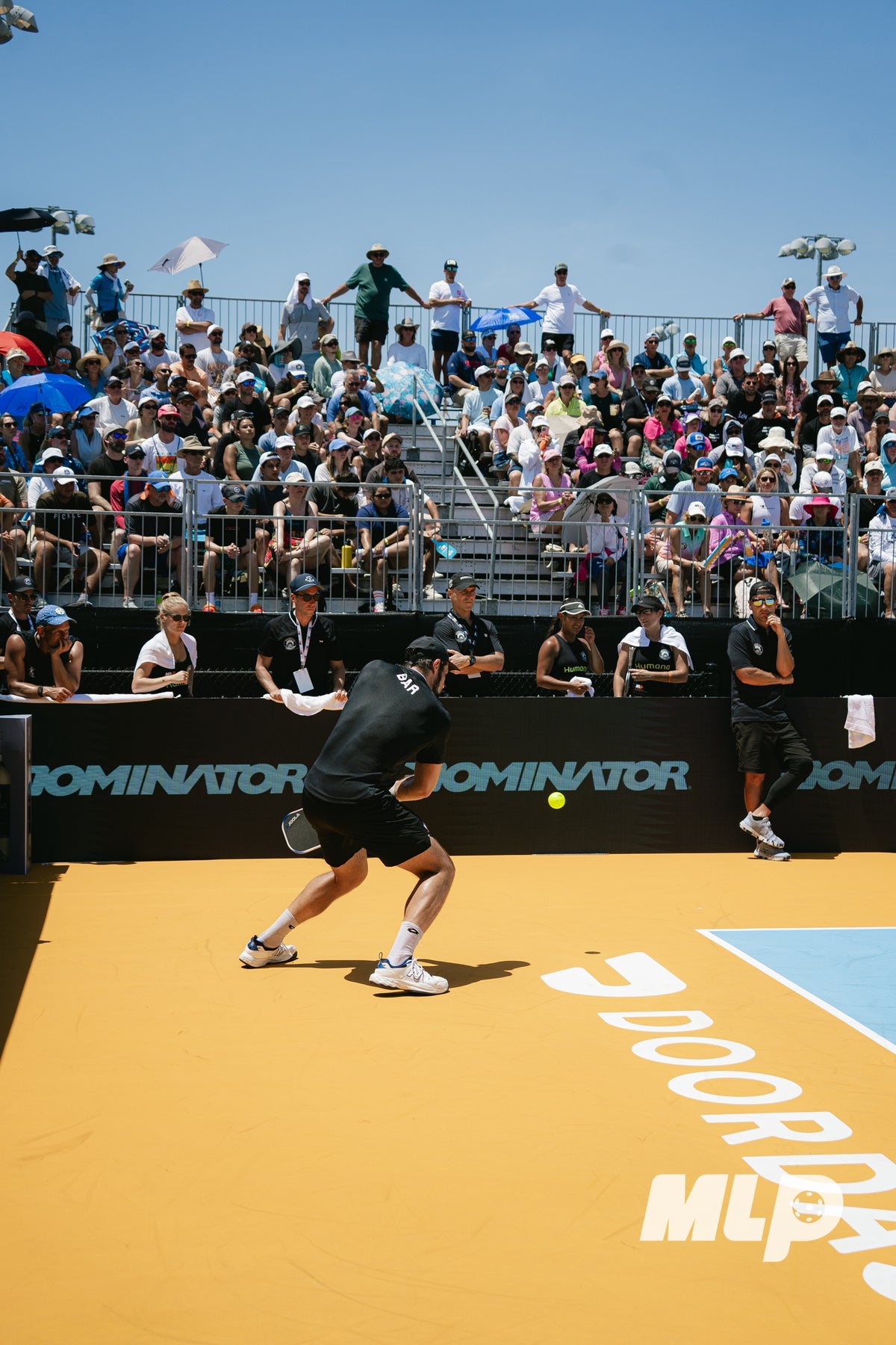 A pickleball player returns a shot in front of spectators and Dominator courtside branding