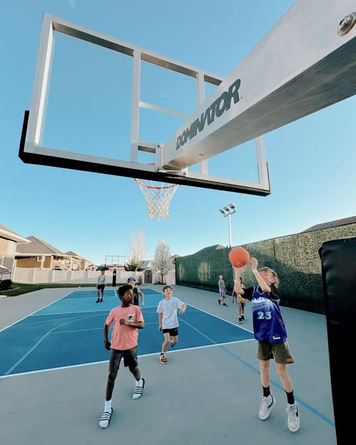 Kids playing basketball under a Dominator hoop on a blue outdoor court
