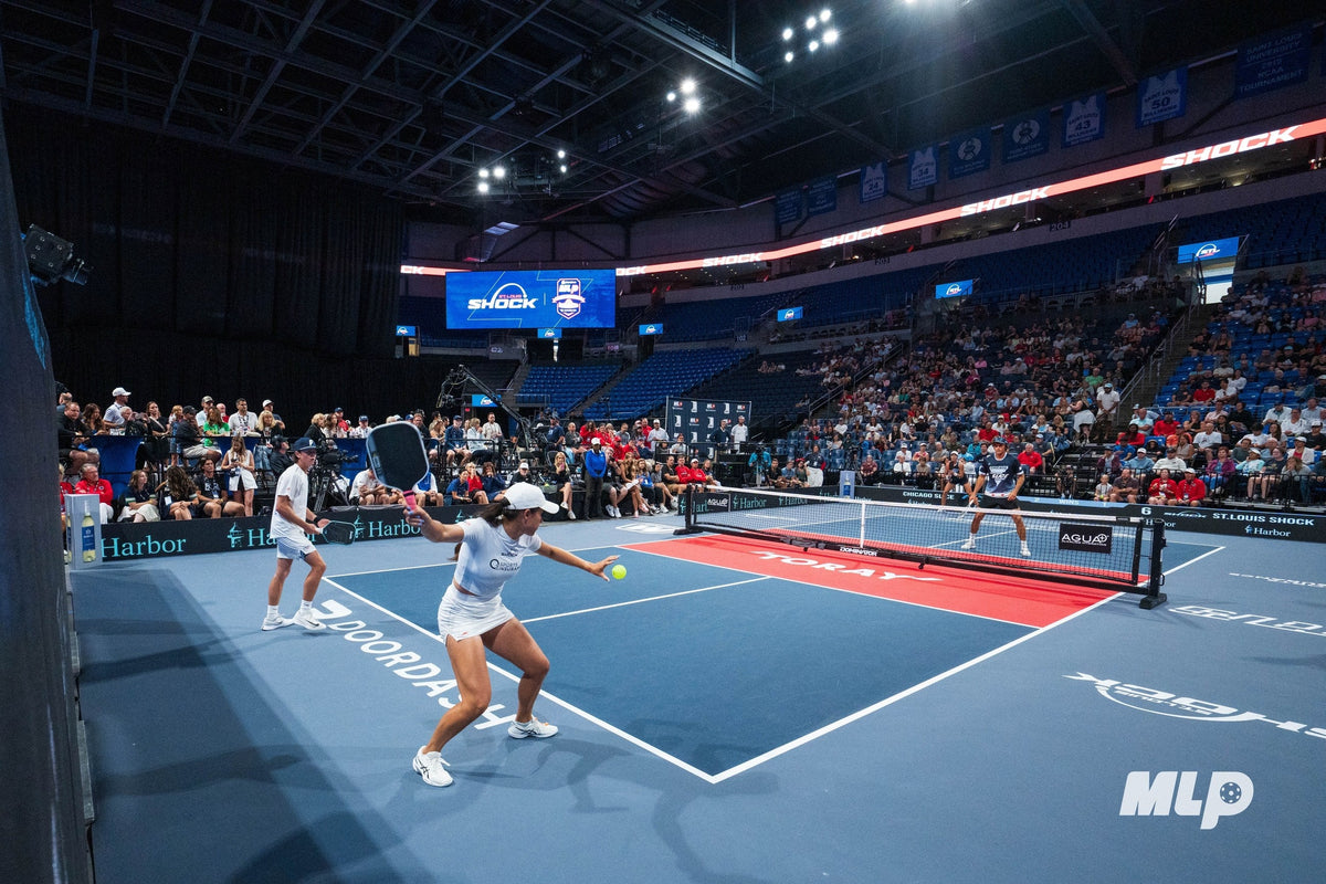 Professional pickleball players compete across a Dominator net in a packed arena