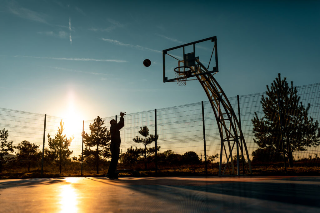 Man shooting a basketball in his fenced backyard basketball court