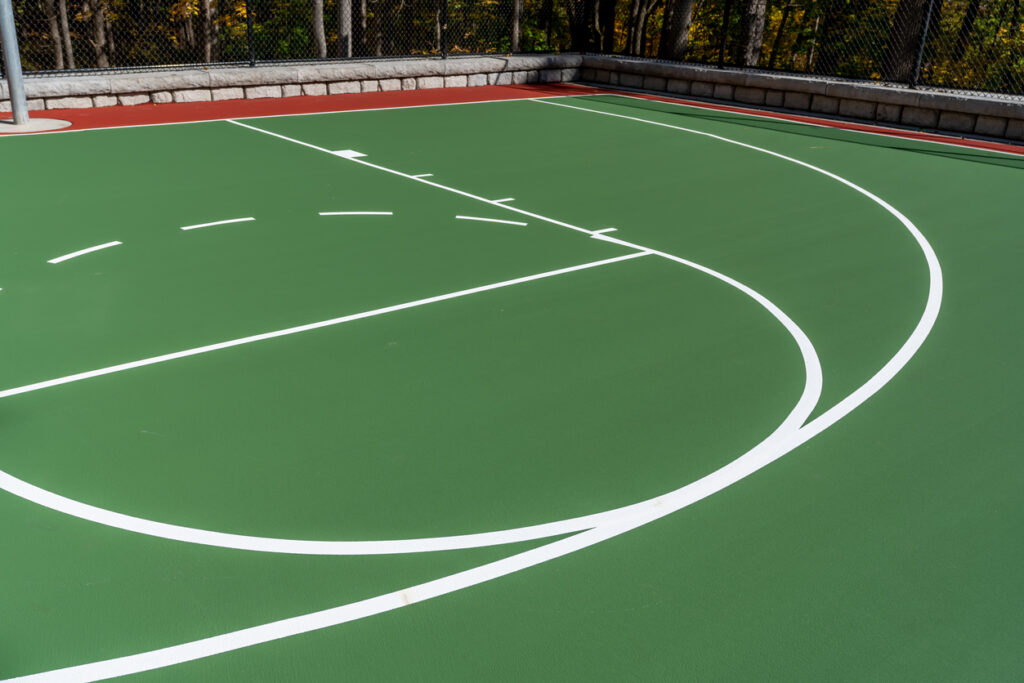A backyard basketball hoop with a green multi-sport surface